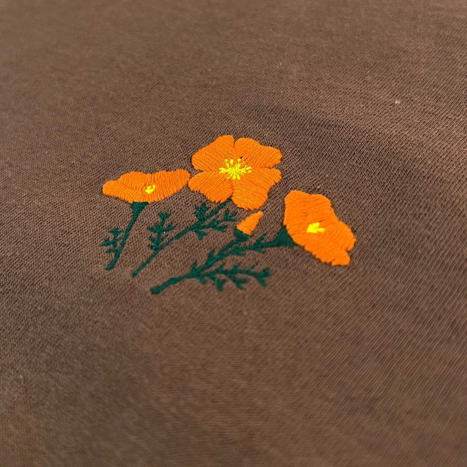 Altru, Small Poppy Embroidery on a brown shirt. close up Poppy